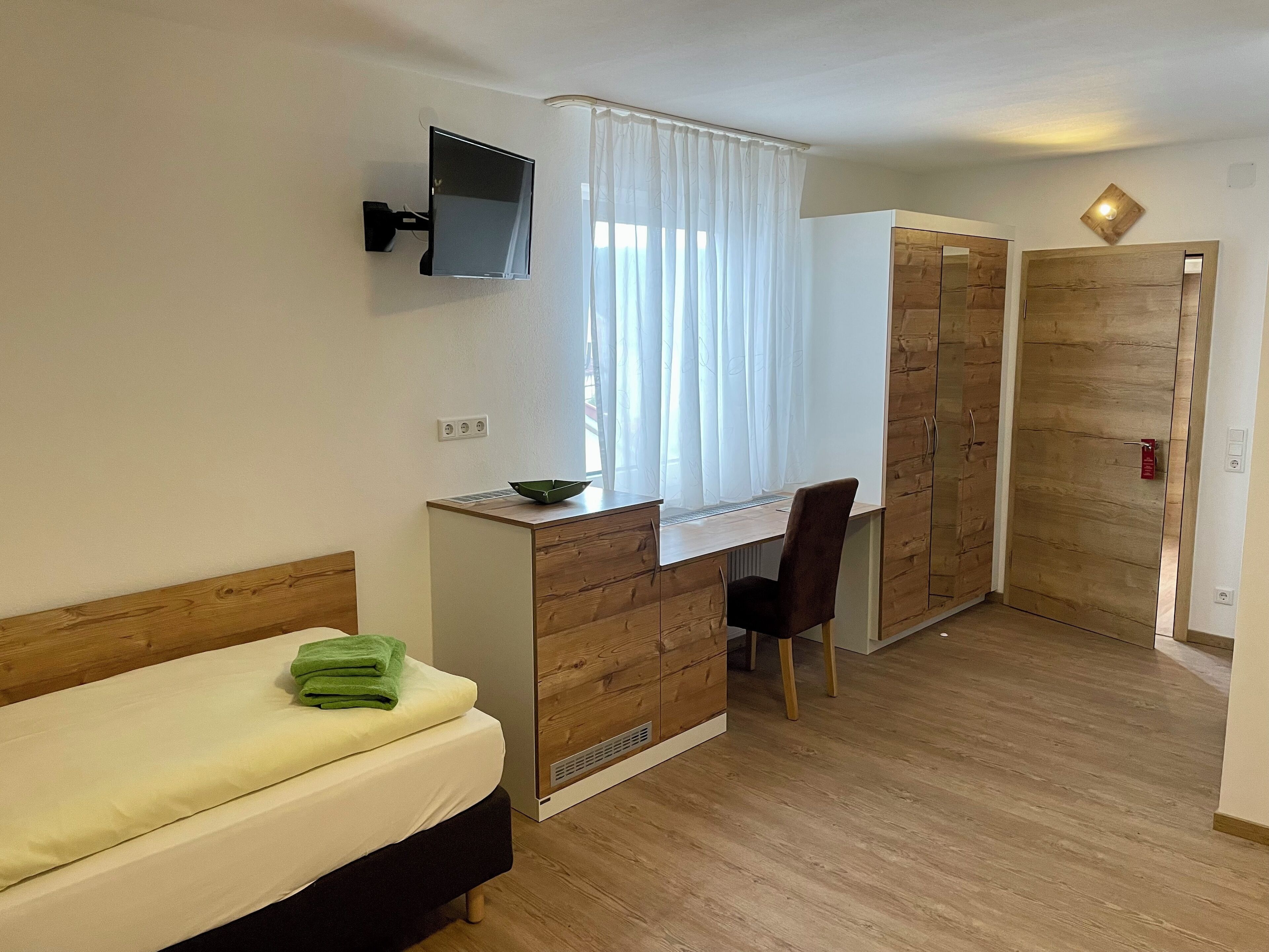A bedroom with a bed, a desk, a chair, a TV, and a wardrobe.