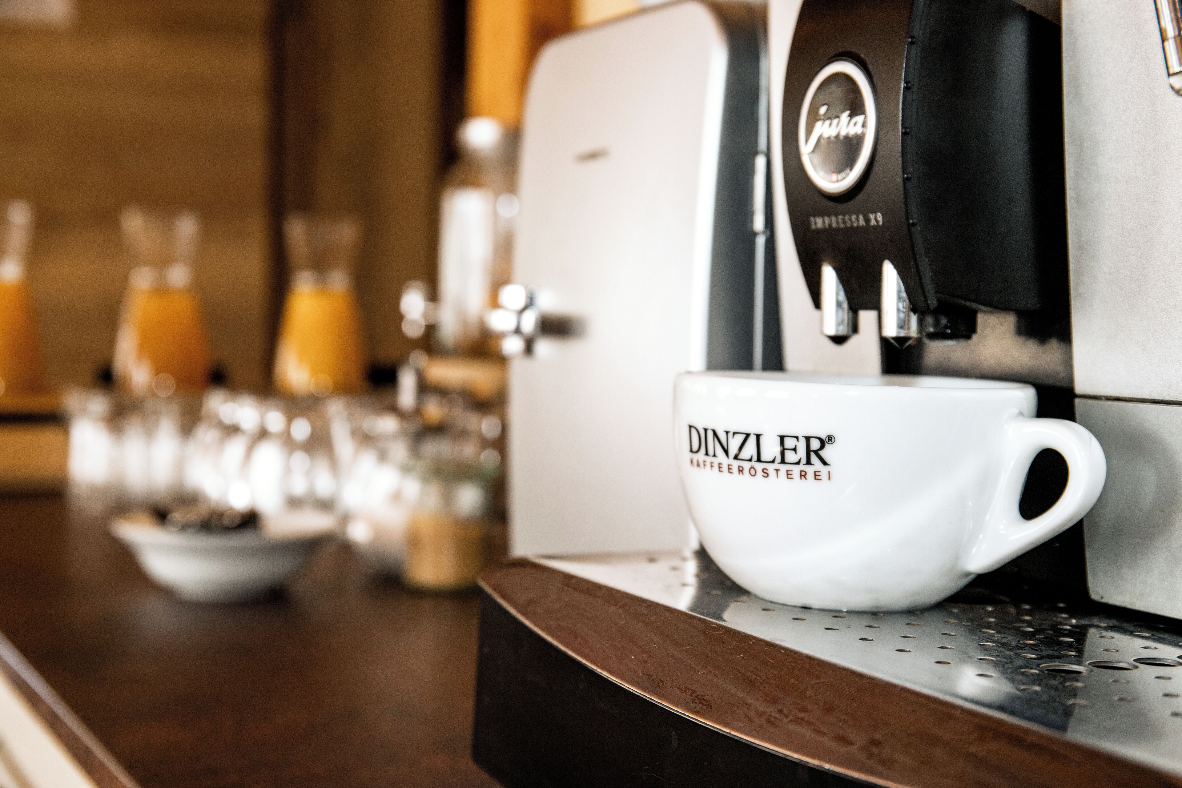 Une machine à café, une tasse à l’effigie de la marque et un verre de jus d’orange sont posés sur un comptoir en bois.