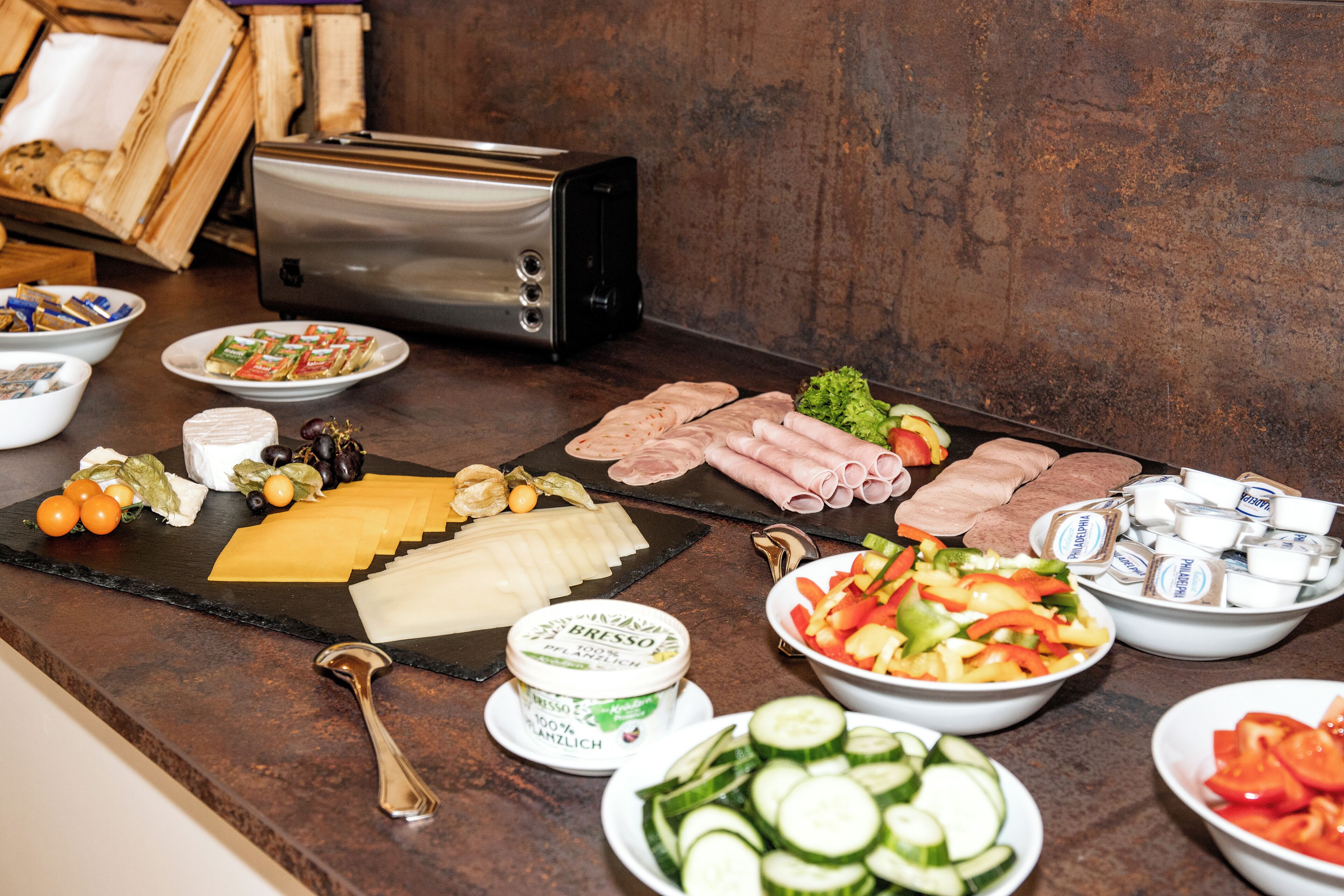 A buffet table with various food items including cheese, meats, vegetables, and condiments.