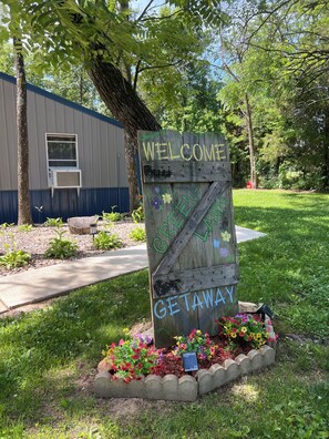 A wooden welcome sign with 'WELCOME' and 'GETAWAY' painted on it, surrounded by a flower bed.