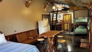 A rustic cabin interior with a wooden dining table, a sofa, a bunk bed, and deer antlers on the wall.