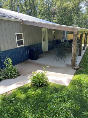 A covered patio area with outdoor seating, a trash bin, and a door leading to the building.