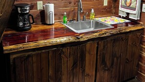 A kitchen with a wooden countertop, a coffee maker, a sink, and a clock on the wall.