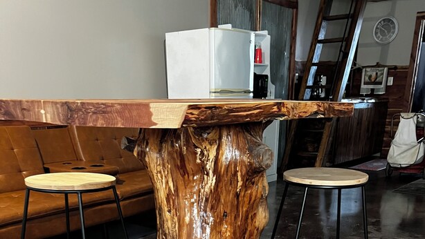 A dining table with a unique wooden base, two stools, and a refrigerator in the background.