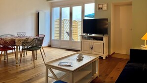 A living room with a dining area, a television on a cabinet, and a view through a glass door.