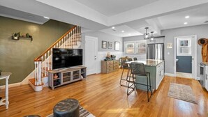 A spacious living room with a wooden floor, a large flat-screen TV, a staircase, and a kitchen area with a bar. - 3BR Salem Townhouse Minutes to downtown (Salem)