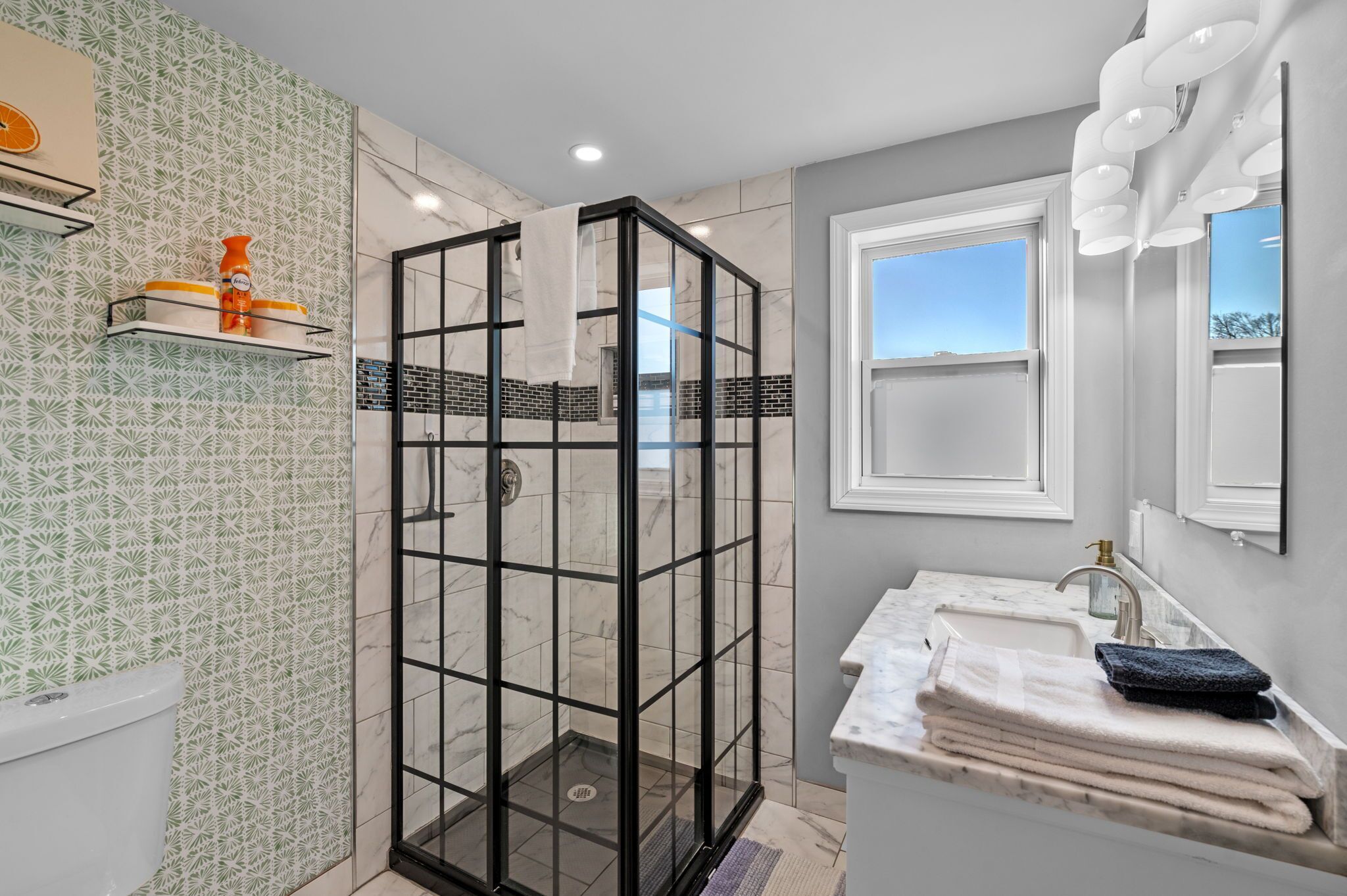 A modern bathroom with a glass-enclosed shower, a marble sink, and patterned wall tiles.
