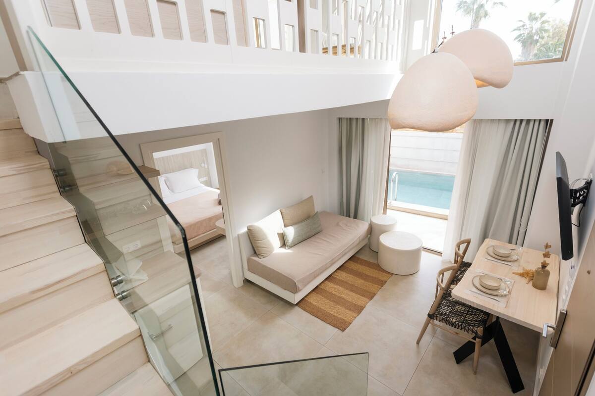 Camera d'hotel moderna con scala in vetro, divano letto, zona pranzo e vista sulla piscina.