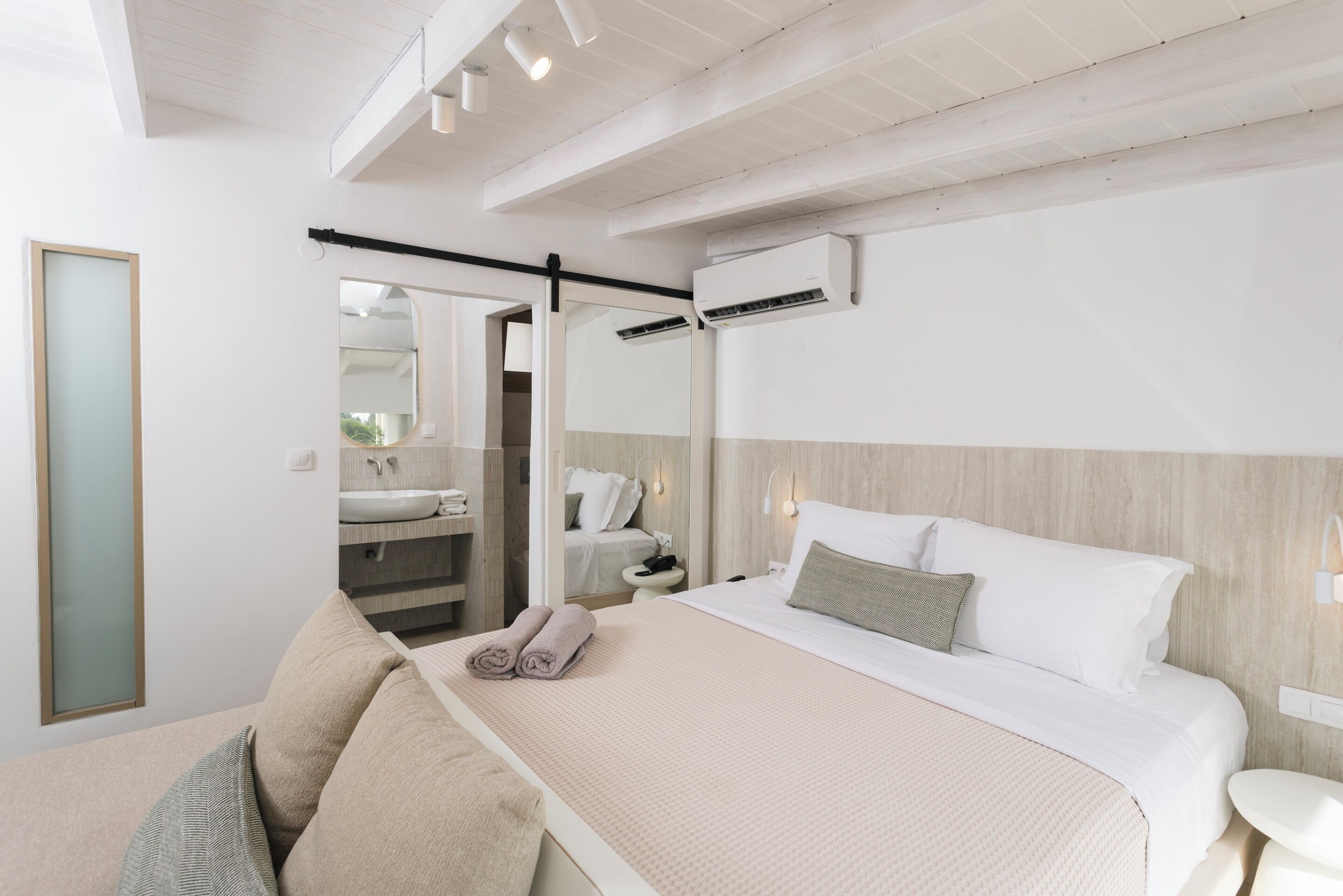 Habitación de hotel moderna con una cama grande, un área de descanso con sofá, una mesita y un baño visible a través de una puerta abierta.