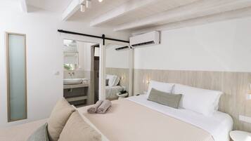 Habitación de hotel moderna con una cama grande, un área de descanso con sofá, una mesita y un baño visible a través de una puerta abierta.