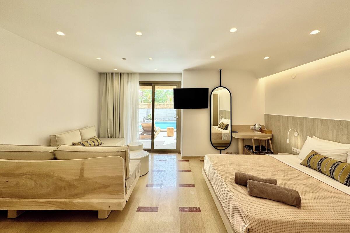 Una camera d'albergo con un letto, un divano, una TV, uno specchio e vista su una piscina all'aperto.