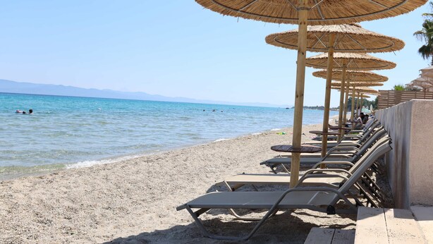 Een strand met ligbedden en rieten parasols.