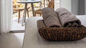 Een hotelkamer met een bed, een rieten mand met handdoeken, een tafel, stoelen en uitzicht op een tuin met een palmboom.