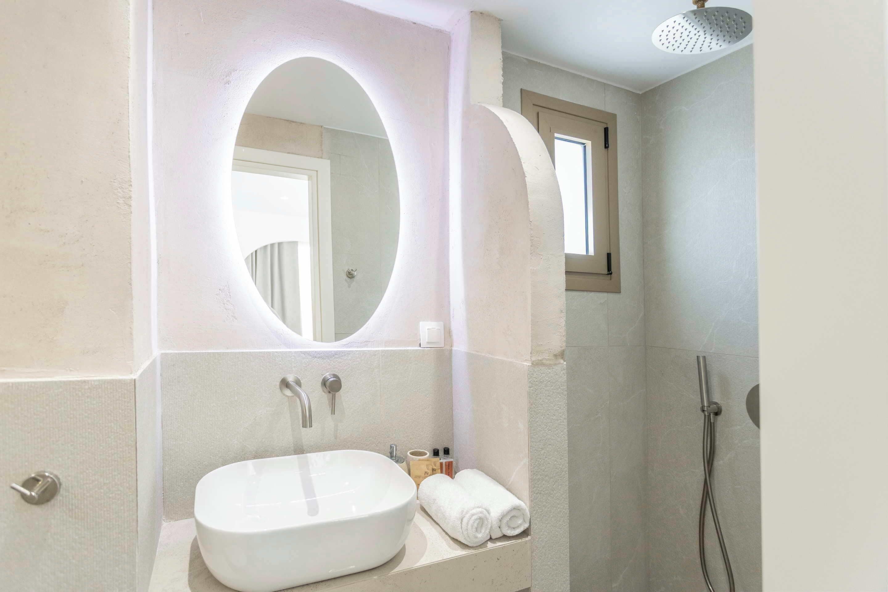 Un baño con un espejo ovalado grande, un lavamanos y una ducha.