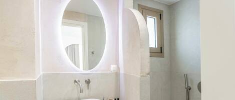 Un baño con un espejo ovalado grande, un lavamanos y una ducha.
