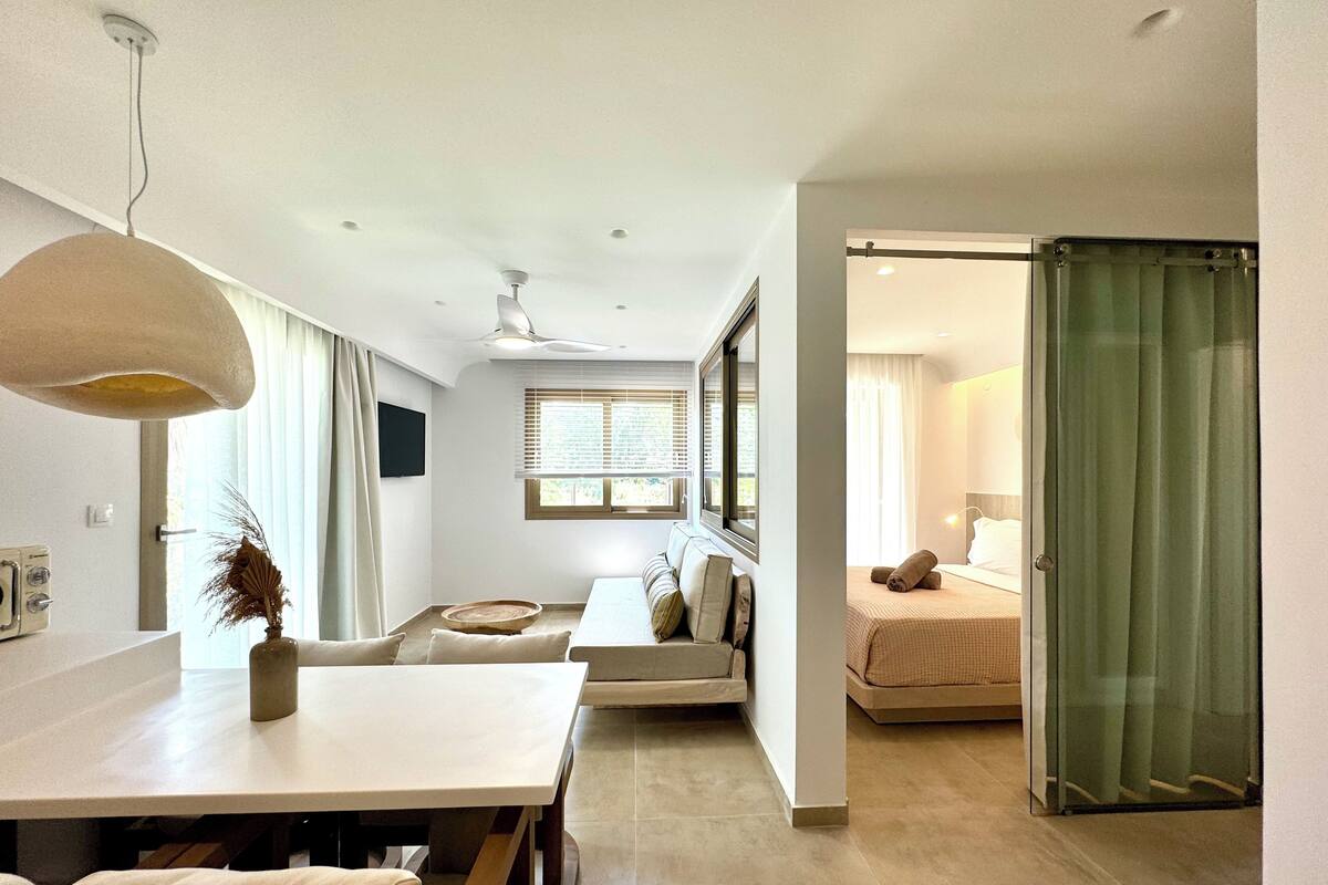 Camera d'albergo moderna con zona pranzo, divano, letto e una porta scorrevole in vetro.