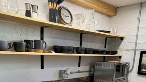Ett kök med vita skåp, en bänkskiva i granit, en mikrovågsugn och en hylla i trä med köksredskap.