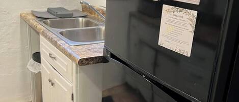 A compact kitchen with a black refrigerator, a sink, and a small countertop.