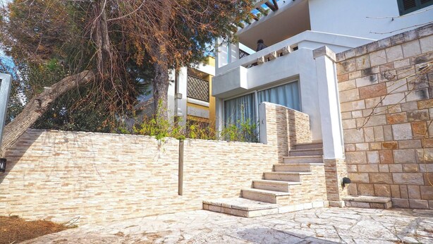 Un edificio moderno con fachada de piedra, un conjunto de escalones de piedra que conducen a una puerta, y un árbol al fondo.