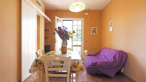 Un comedor con una mesa dispuesta para cuatro personas, un sofá cubierto con púrpura y un jarrón de flores sobre la mesa.
