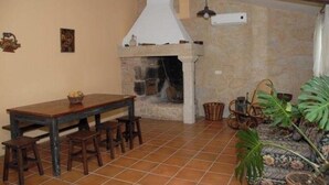 Un interior rústico con chimenea de piedra, mesa y bancos de madera, y una planta grande en maceta.