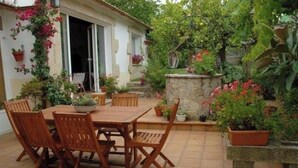 A patio with a wooden table and chairs, surrounded by potted plants and a stone wall. - Casa da Pesqueira [with garden 80 meters from the c] en Cabo de Cruz - Boiro (Cabo de Cruz)