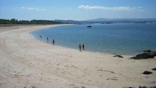 Una playa amplia de arena con aguas tranquilas y algunas personas.