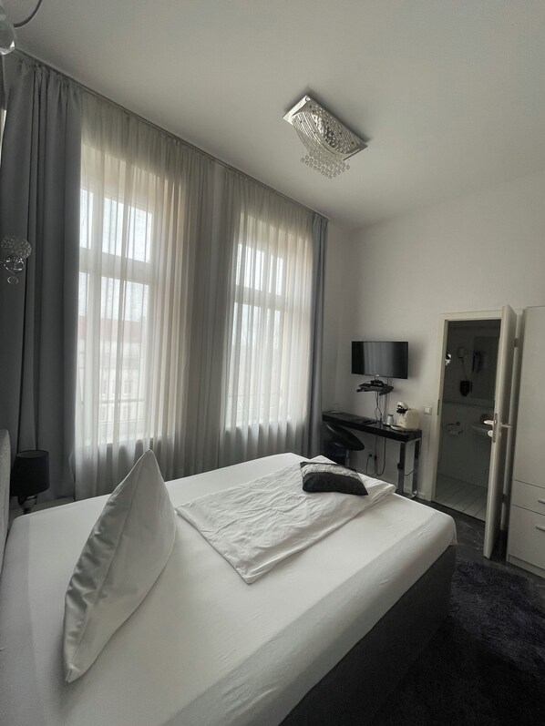A hotel room with a bed, a desk, a chair, a television, and a bathroom door. - Maison LeMi (Altenburg)