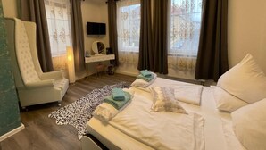 Quarto de hotel com uma cama grande, uma cadeira, uma televisão e uma janela com cortinas.