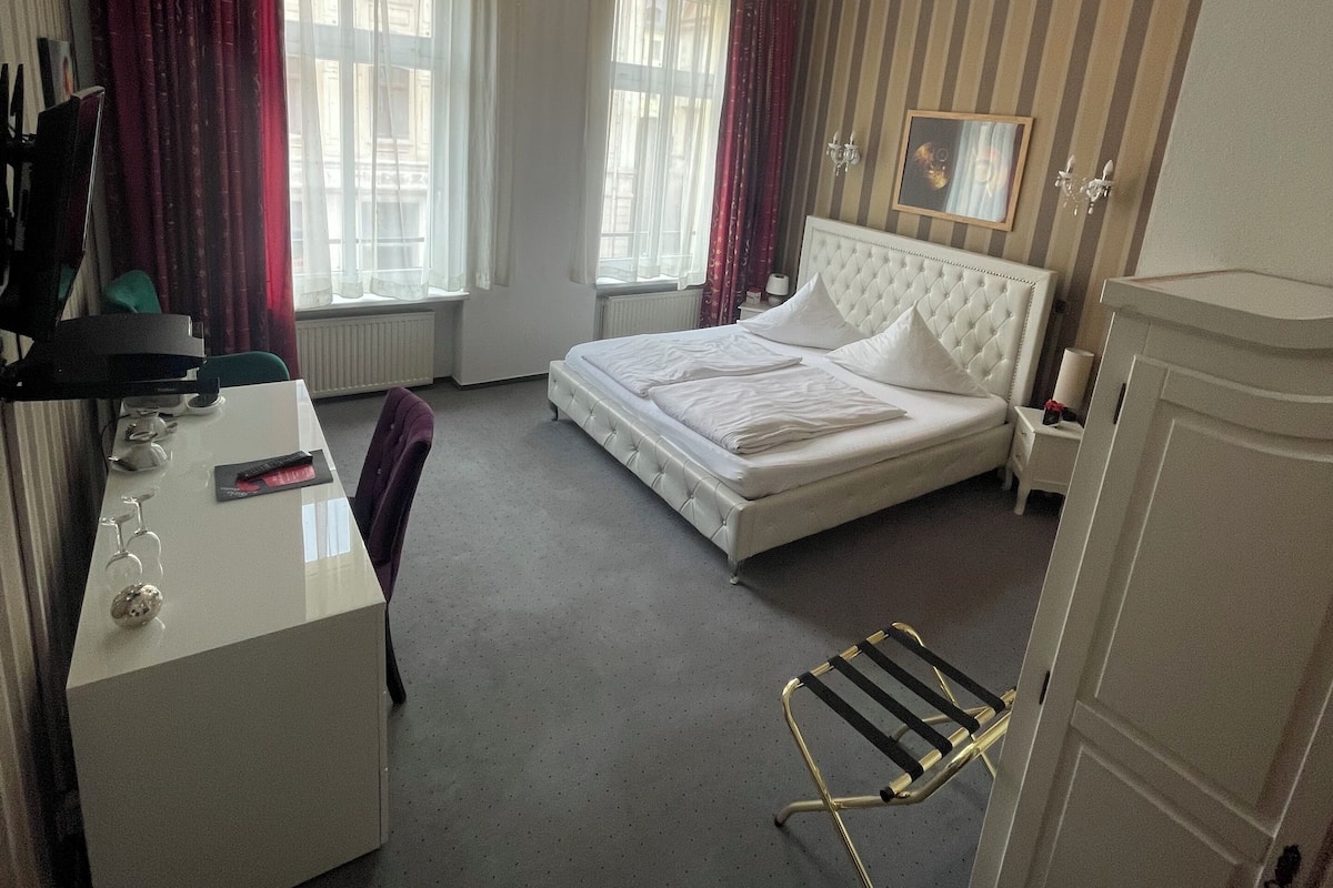 Ein Hotelzimmer mit Bett, Schreibtisch, Stuhl, Kleiderschrank und einem fensterbepflanzten Fenster.