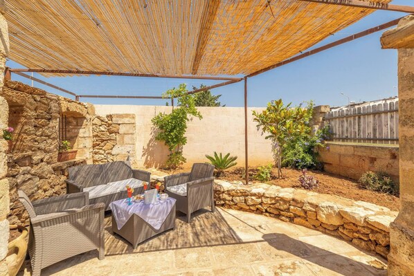 An outdoor patio with wicker furniture, a table, and a stone wall.