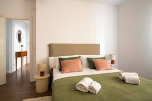 Ein Hotelzimmer mit Bett, Kissen, Nachttisch, Lampe, Spiegel und einer grünen Decke.