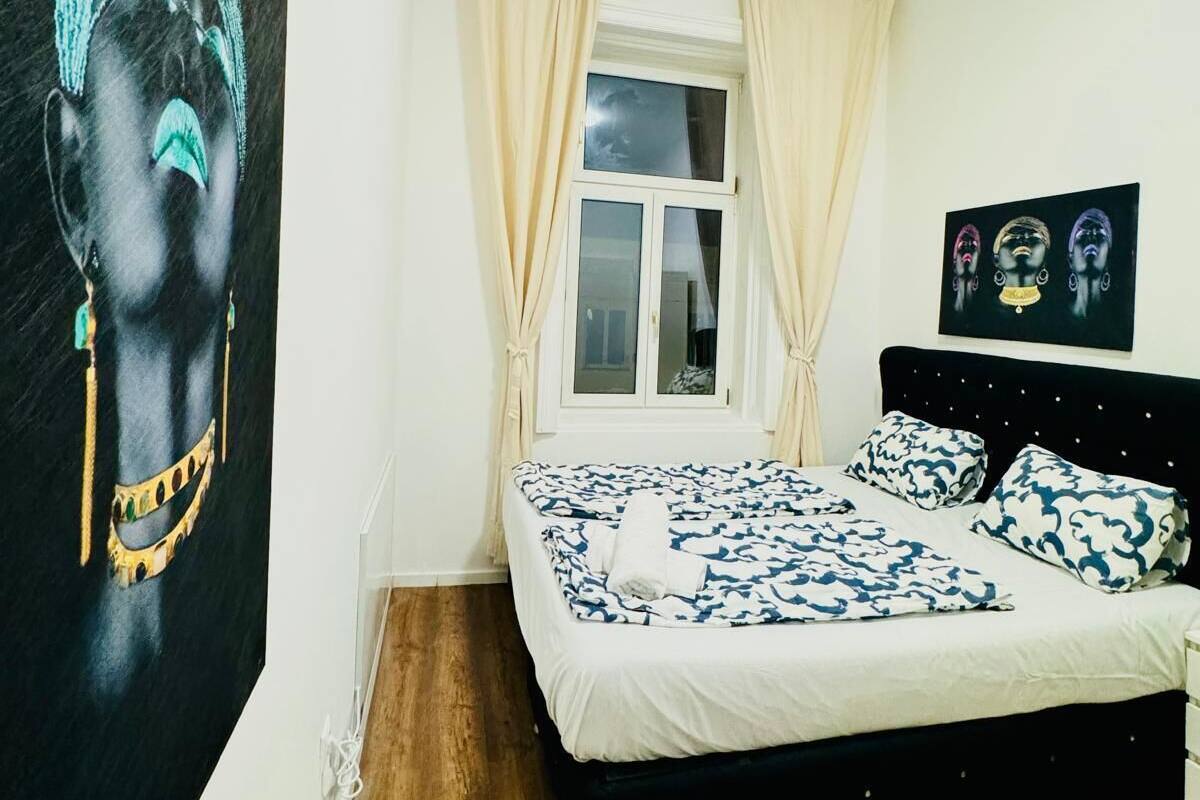 Ein Schlafzimmer mit einem Bett, einem Fenster mit Vorhängen, einem Bild an der Wand und einem gerahmten Foto über dem Bett.