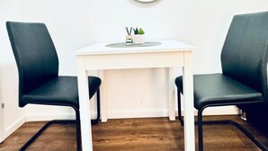 Ein kleiner, weißer Schreibtisch mit zwei schwarzen Stühlen, ein runder Spiegel an der Wand und eine kleine Pflanze auf dem Schreibtisch.