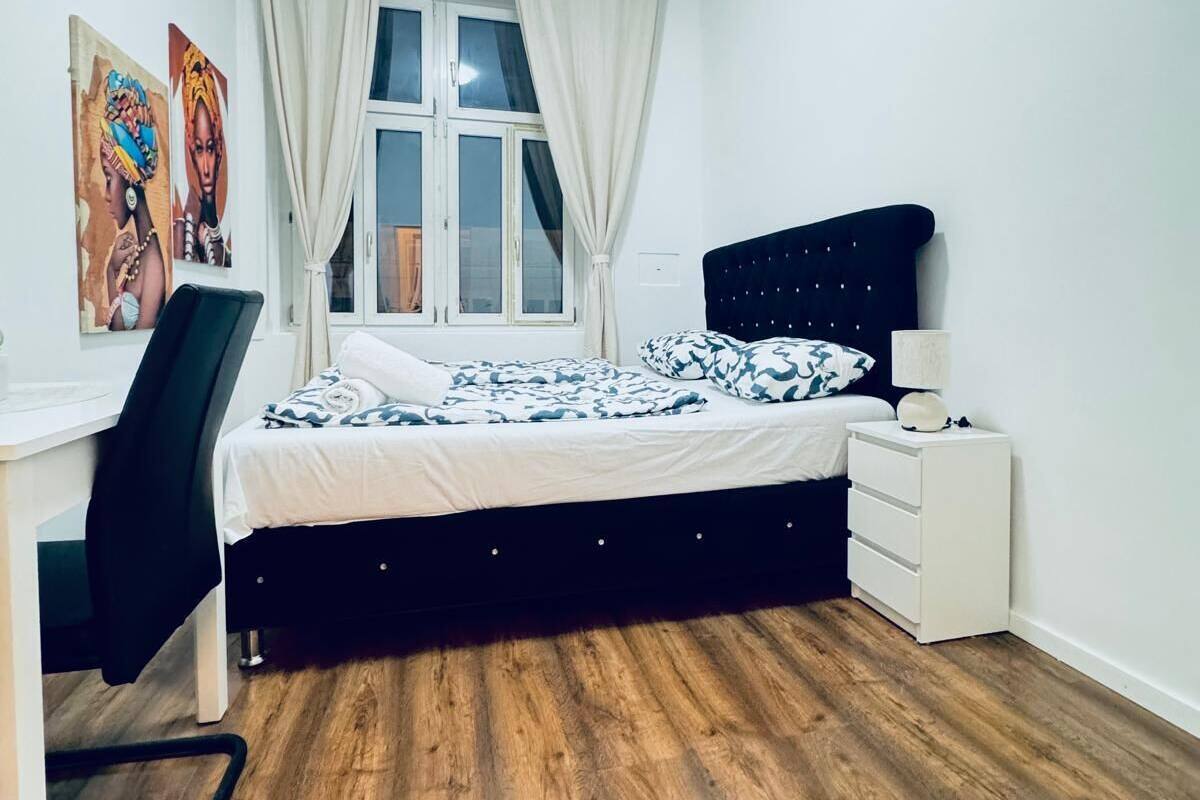 Ein Schlafzimmer mit Bett, Schreibtisch, Stuhl, Nachttisch und einem Fenster mit Vorhängen.