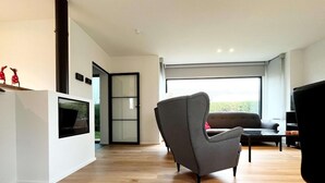Ein modernes Wohnzimmer mit einem grauen Sessel, einer Couch und einem flachbildschirmfernseher, der an einer weißen Wand angebracht ist.