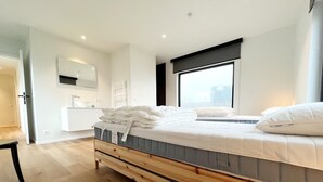 Ein modernes Schlafzimmer mit einem hölzernen Bett, einem großen Fenster und einem minimalistischen Badezimmer.