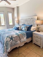 Quarto com cama, mesas de cabeceira, ventoinha no teto e janela com persianas.