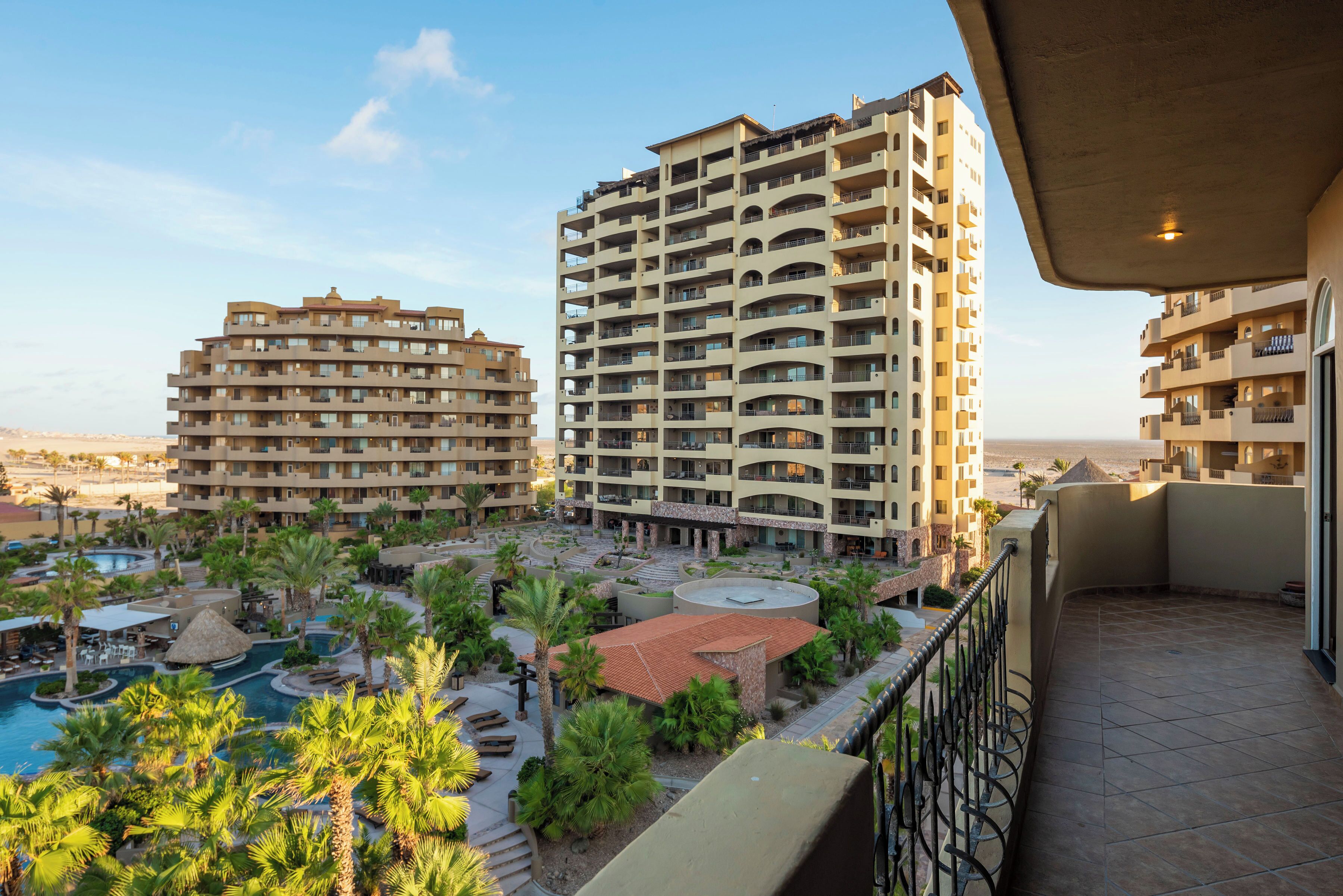 A hotel with multiple floors, a swimming pool, and a courtyard with palm trees.