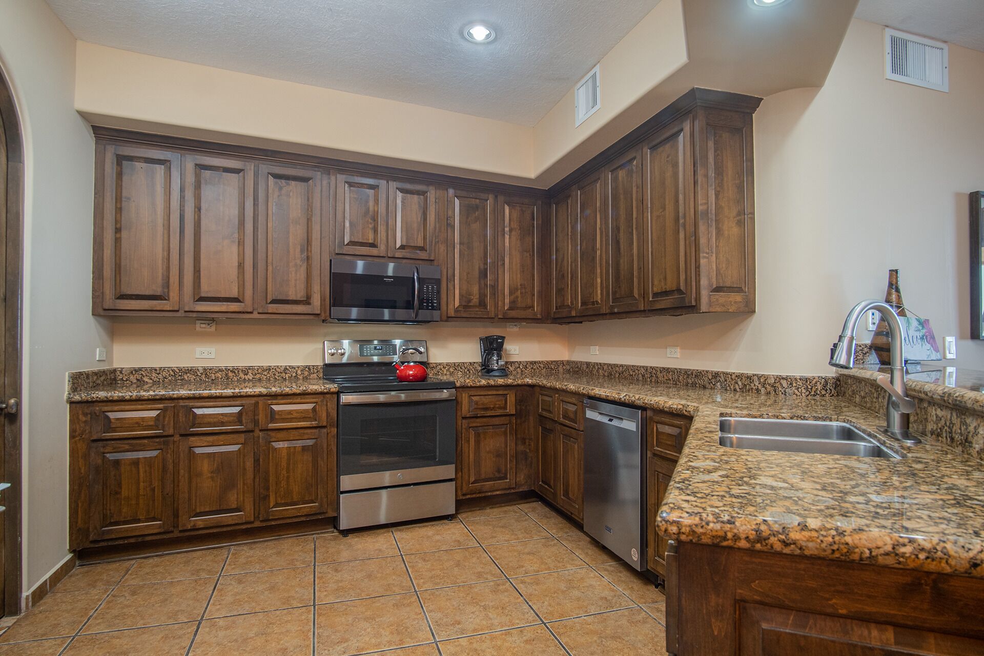 A kitchen with wooden cabinets, stainless steel appliances, granite countertops, and a tiled floor.