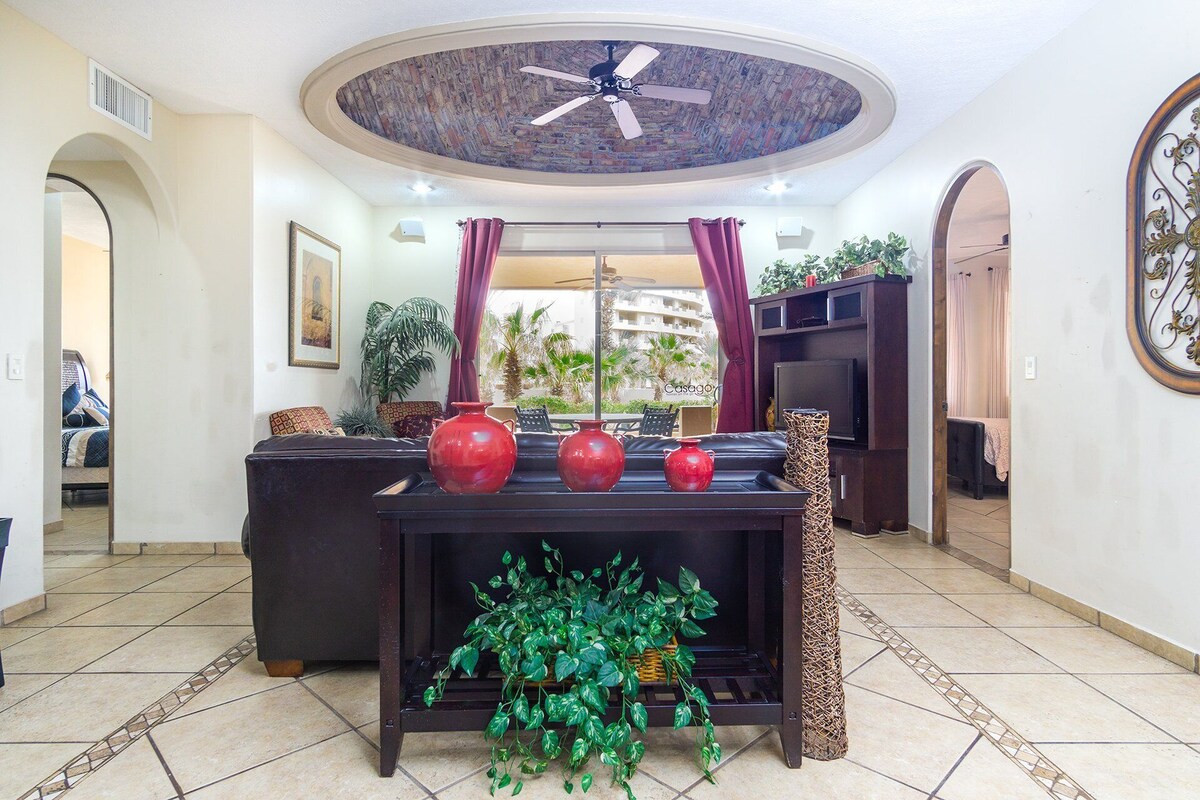 A living room with a ceiling fan, a TV on a wooden stand, and a large window with curtains.