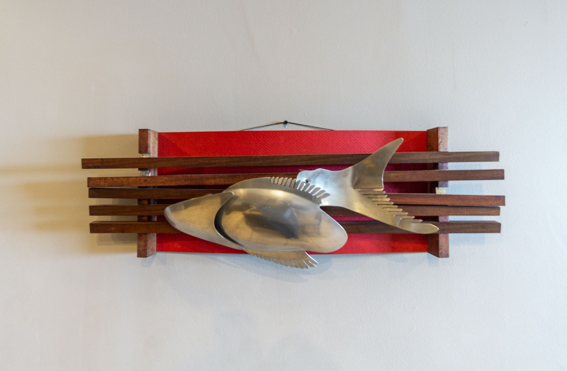 Una escultura de un pez montada en la pared, sobre un banco rojo y marrón.