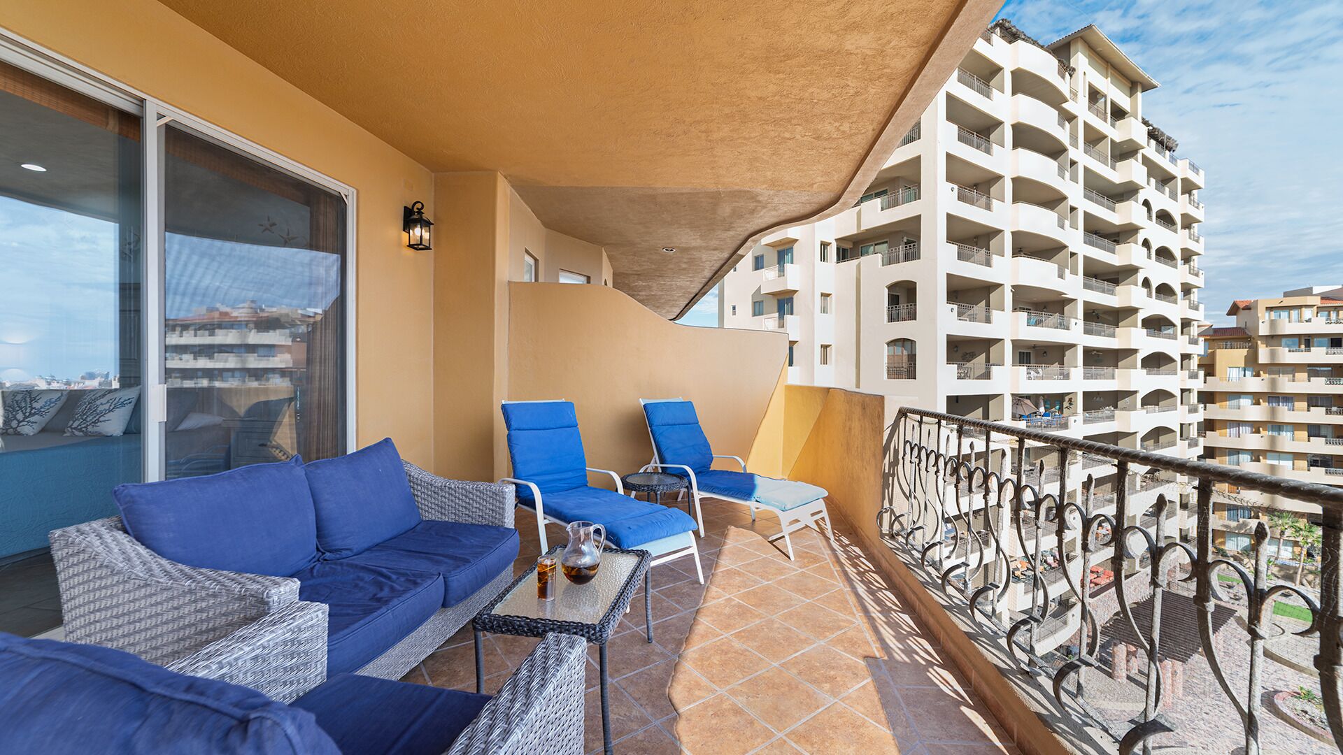 A balcony with blue cushioned chairs, a wicker table, and a glass door leading to a terrace.