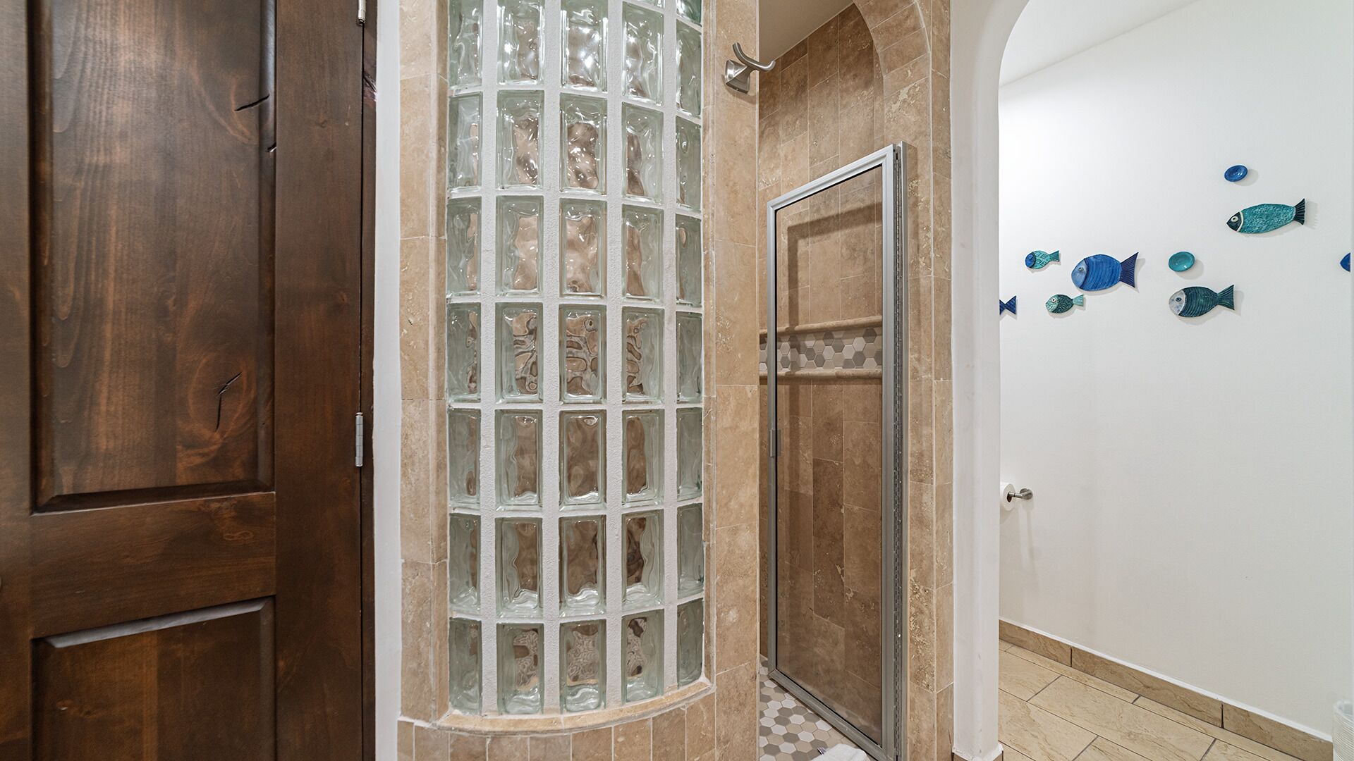 A bathroom with a glass shower enclosure, a wooden door, and decorative fish wall art.