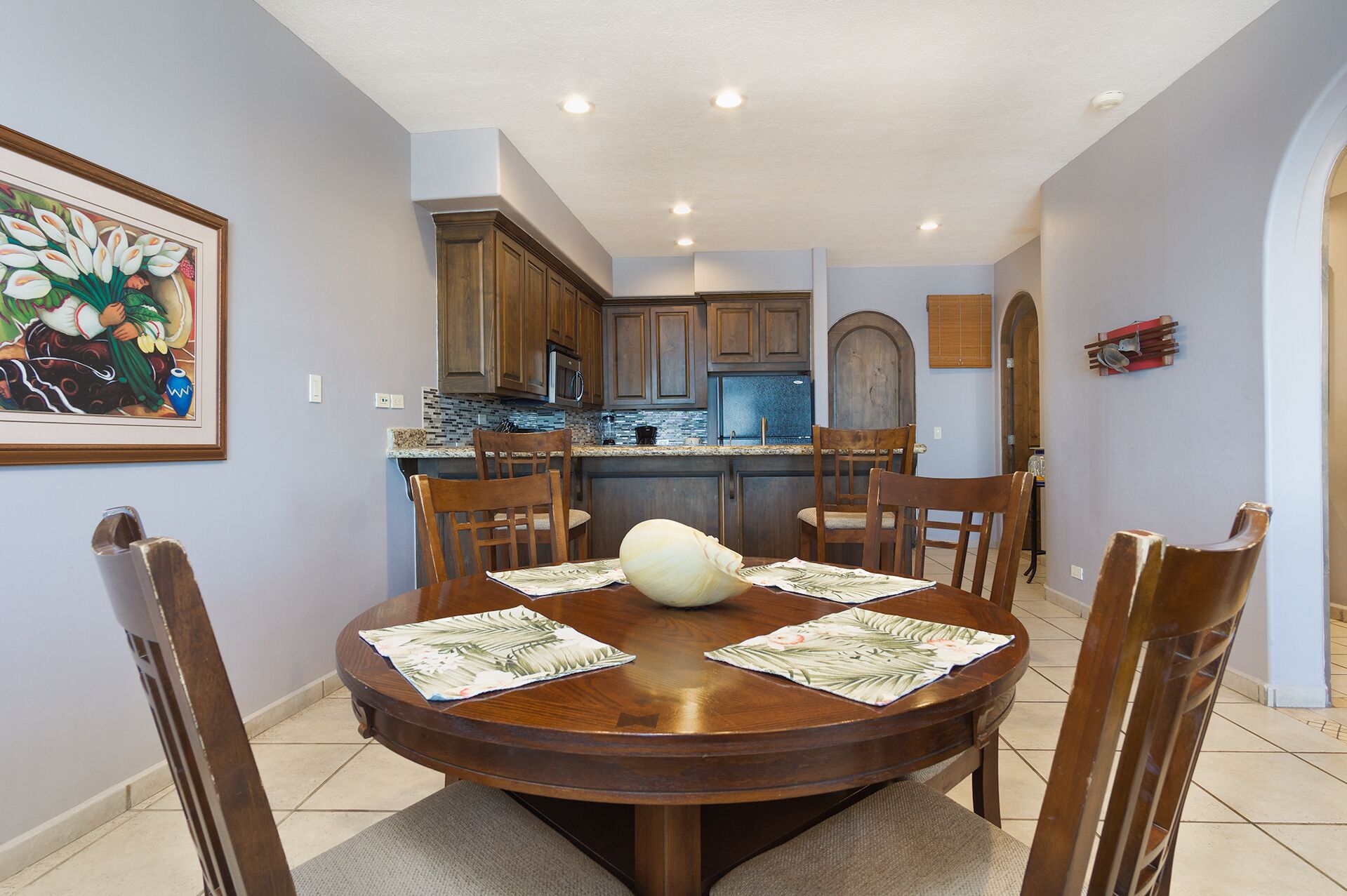A dining area with a round wooden table, six chairs, and a central white vase.