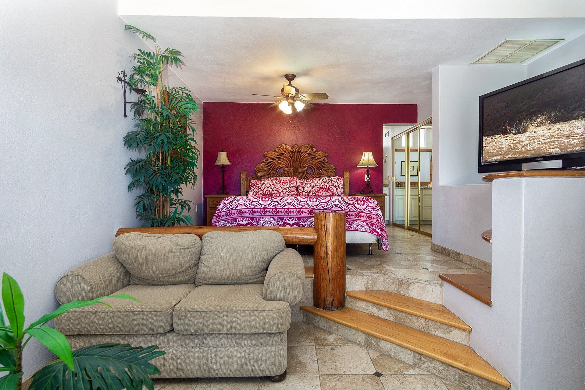 A bedroom with a bed, a wooden headboard, a ceiling fan, a TV, and a staircase.
