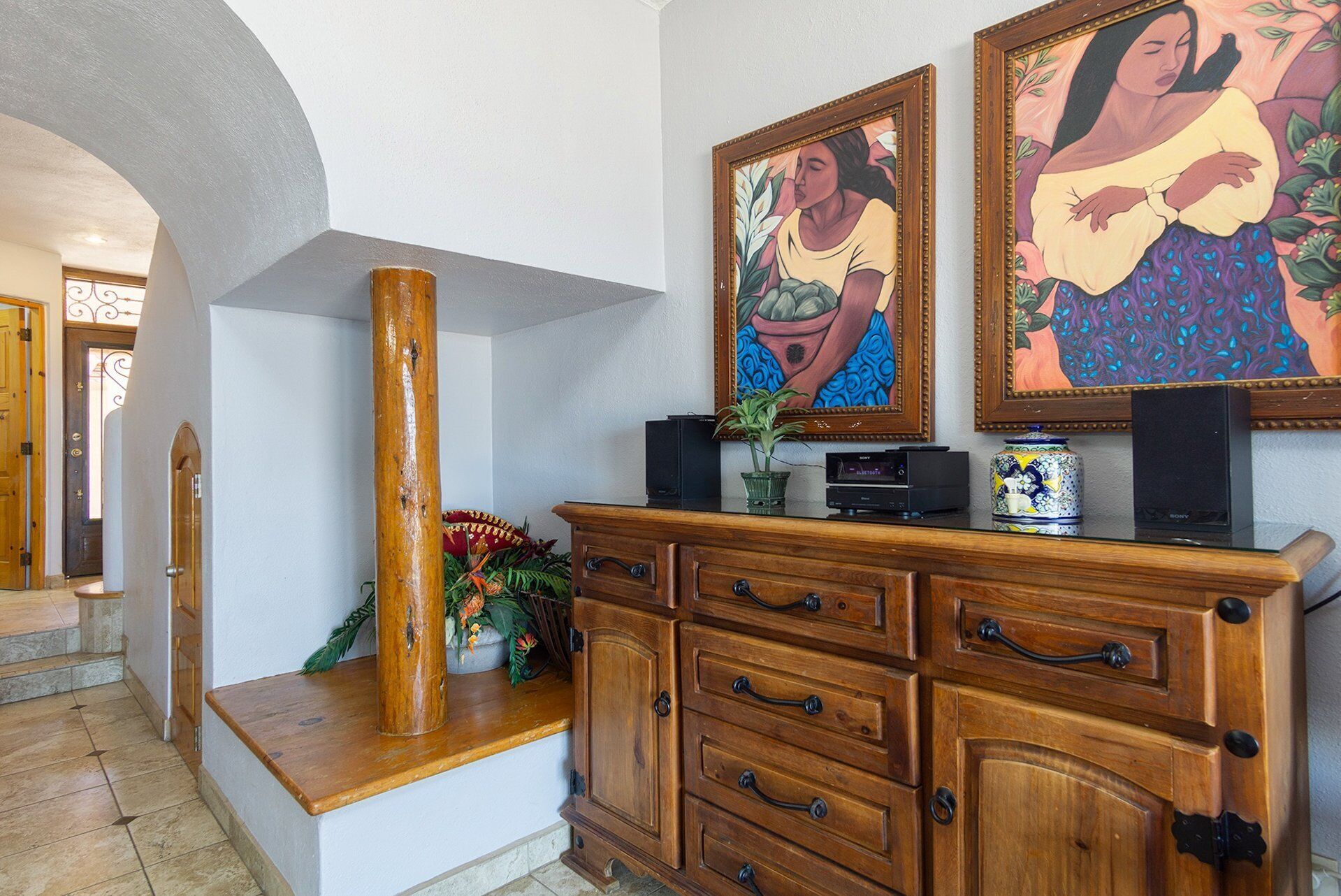 A wooden cabinet with drawers, a tall wooden pillar, and two framed paintings on the wall.