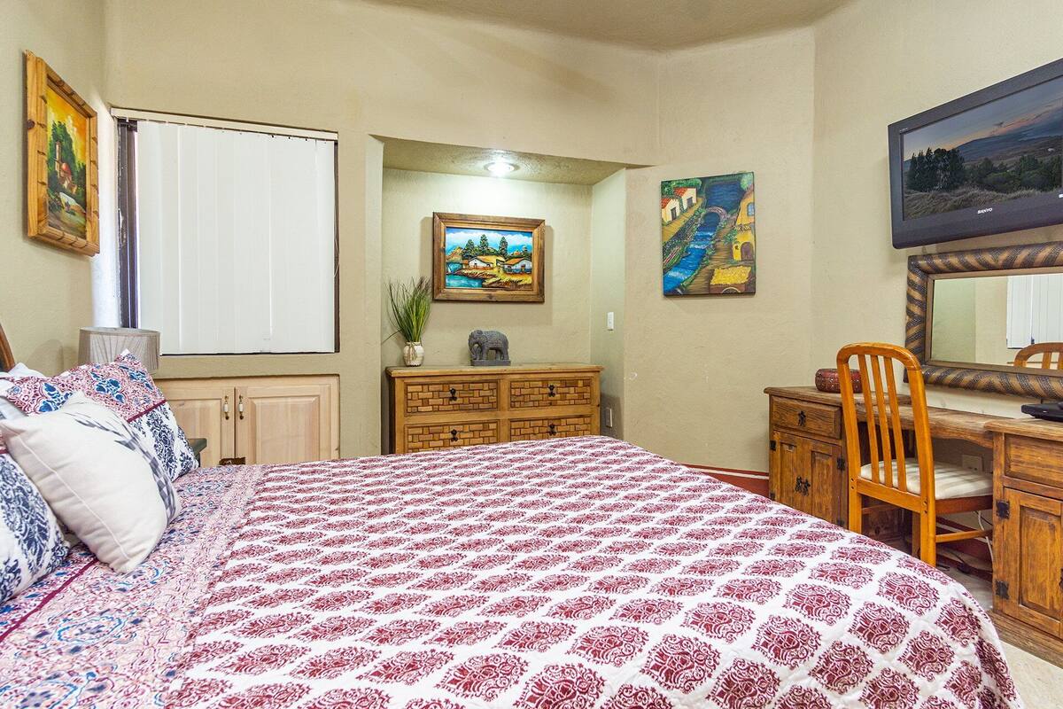 A bedroom with a bed, dresser, chair, and paintings on the walls.