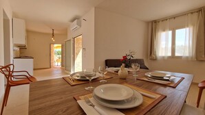 Ein Essbereich mit einem Holztisch, gedeckt für vier Personen, einer Küche im Hintergrund und Blick ins Freie durch eine Schiebetür.