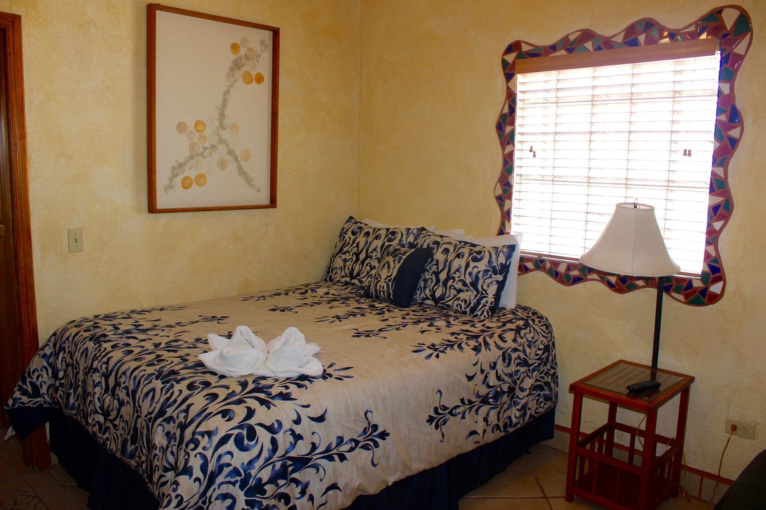 A hotel room with a bed, a bedside lamp, and a window with a decorative frame.